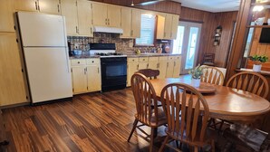 Une cuisine avec des meubles de rangement en bois, une cuisinière, un réfrigérateur et une table à manger avec des chaises.
