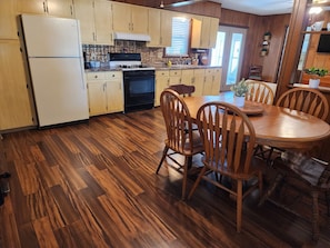A kitchen with wooden cabinets, a stove, a refrigerator, and a dining table with chairs.