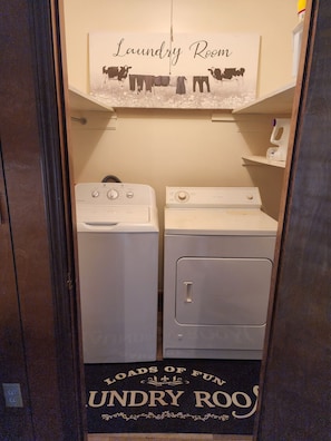 A laundry room with two washing machines, a sign above stating 'Laundry Room,' and a sign below reading 'Loads of Fun Laundry Room.'