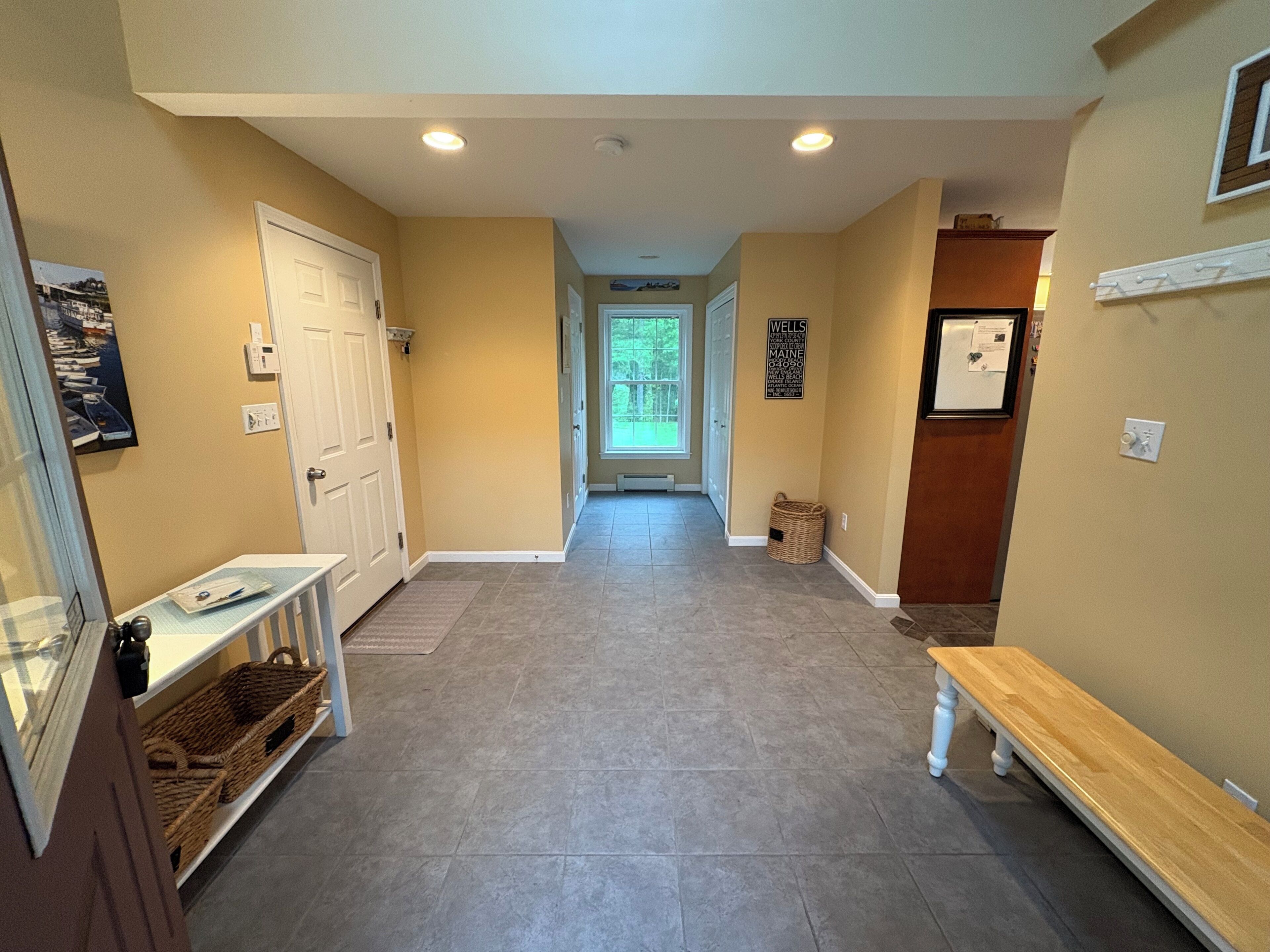 A hallway with a bench, a door, a basket, and a sign on the wall.