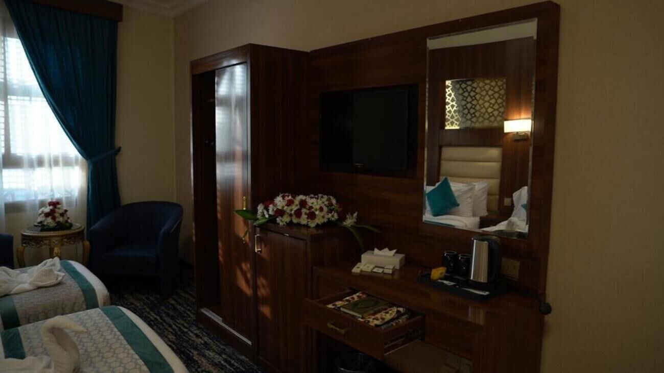 A hotel room with a bed, a TV, a desk with a lamp, a chair, and a window with curtains.