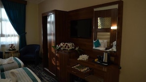A hotel room with a bed, a TV, a desk with a lamp, a chair, and a window with curtains. - Triple One Hotel  (Madinah)