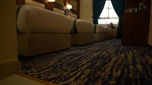 A hotel room with a carpeted floor, a sofa, a wooden cabinet, and a window with curtains. - Triple One Hotel  (Madinah)
