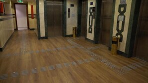 A hallway with wooden flooring, two elevators, and a fire extinguisher. - Triple One Hotel  (Madinah)