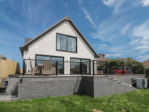 A modern two-story house with a balcony, a brick foundation, and a clear sky. - Puffin Lodge (Filey)