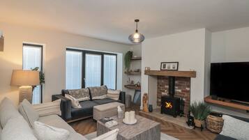 A living room with a sofa, coffee table, fireplace, TV, and large windows.