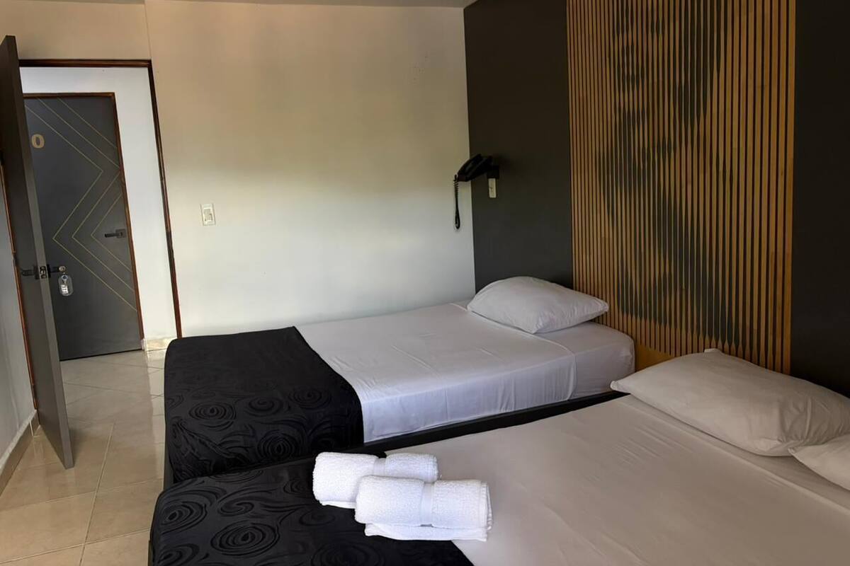 A hotel room with a bed, a bedside table, a wall-mounted phone, and a door.