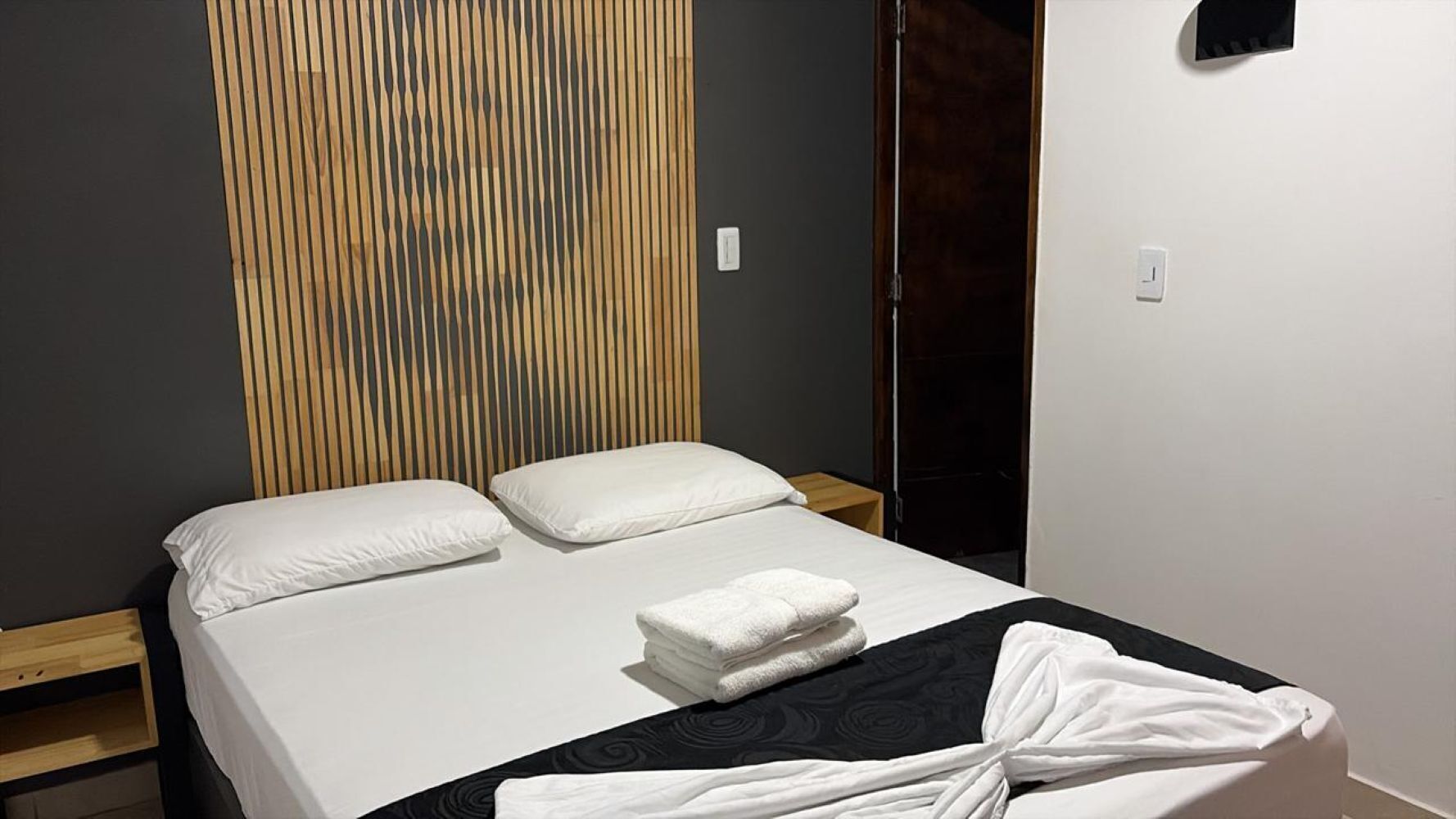 Una cama con ropa de cama blanca, un plaid blanco y negro estampado y una toalla blanca doblada.