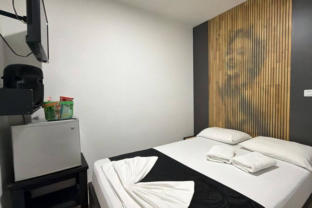 A hotel room with a bed, a desk with a telephone, and a wall-mounted television.