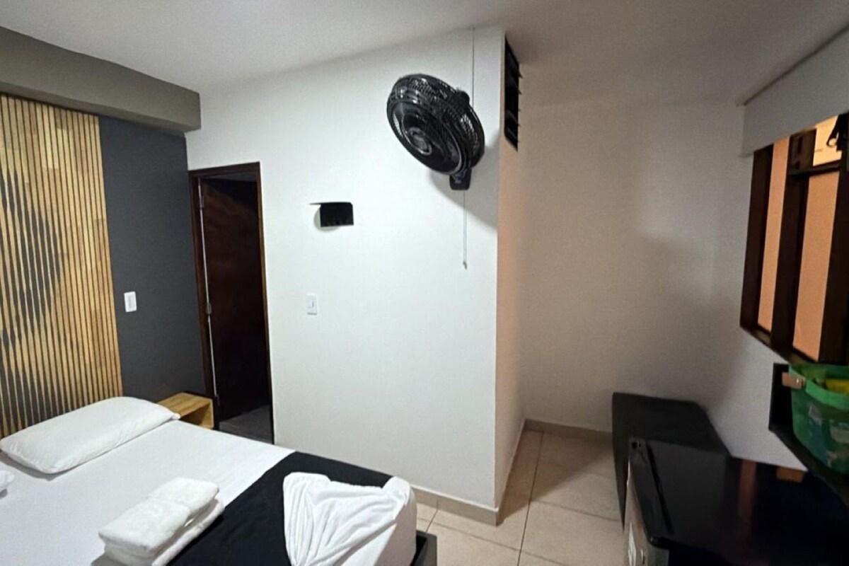 Ein Hotelzimmer mit einem Bett, einem Holz-Kopfteil, einem Wandventilator und einem Fernseher.