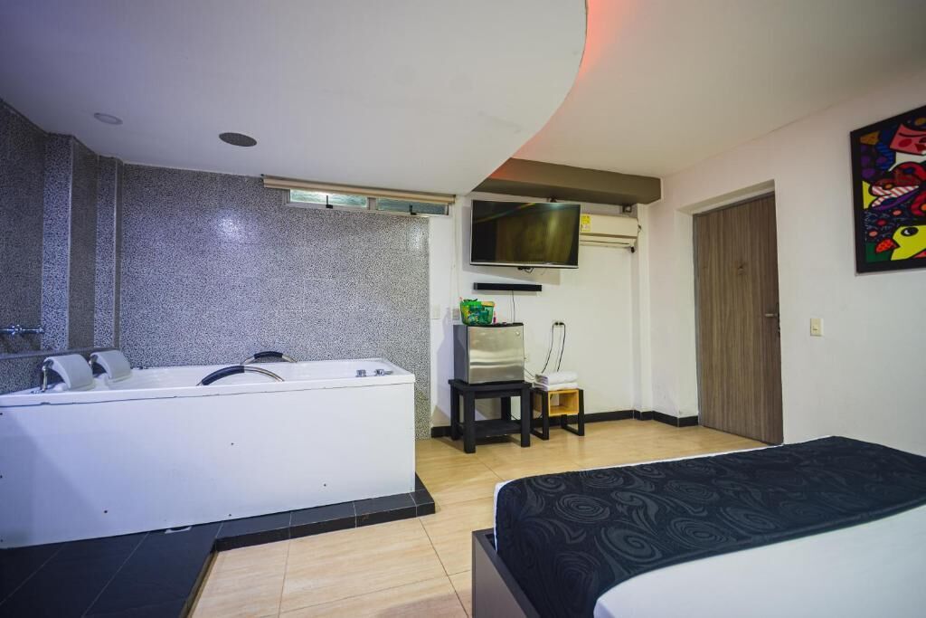 A hotel room with a large bathtub, a bed, a television, and a small table with a chair.