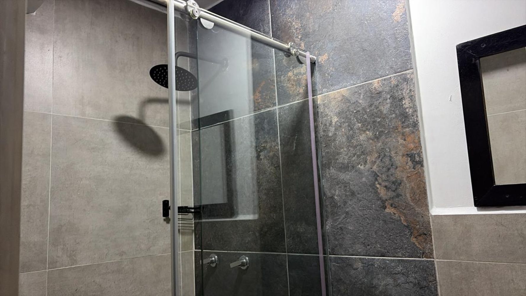 Une douche fermée par des parois de verre, dotée d’un panneau de commande, de murs carrelés et d’un pommeau de douche visible.