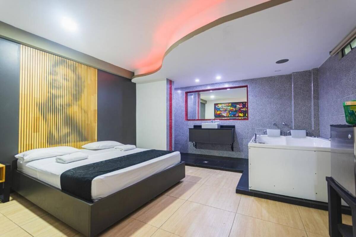 A modern hotel room with a bed, a bathroom with a sink and mirror, and a small kitchen area.