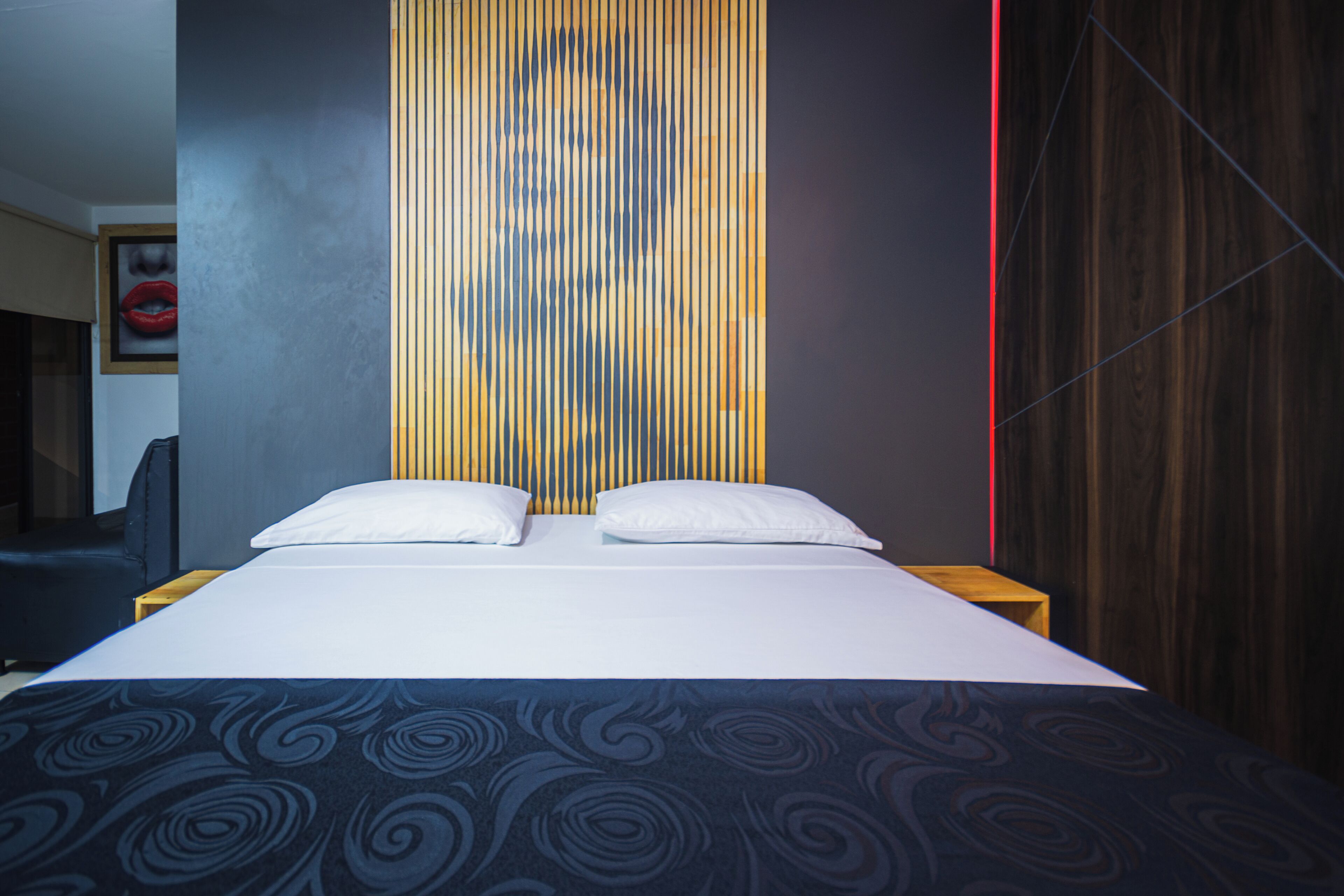Habitación de hotel moderna con una cama grande, pared con rayas verticales y cabecero de madera.