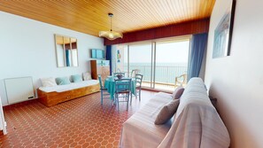 Ein Zimmer mit Holzbalkendecke, einer Couch, einem Esstisch mit Stühlen, einem großen Fenster mit Meerblick und einem Fliesenboden.
