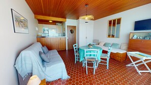 Ein gemütliches Interieur mit Holzbalkendecke, einem Essbereich mit rundem Tisch, einer Couch und einer Küchenzeile.