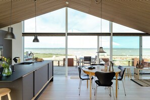 A modern kitchen with a large island, a dining area with a view, and a spacious living area with a high ceiling. - Architect-designed gem with views of Venø Bay (Vinderup)