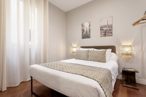 A neatly made bed with a patterned blanket, two wall-mounted lamps, and two cityscape pictures on the wall. - Genteel Home Duque de Osuna II (Madrid)