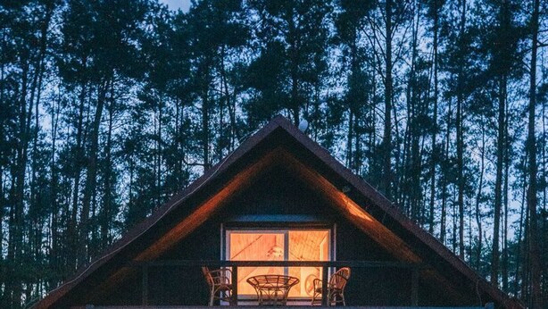 A cabin with a wooden deck, a covered porch, and a large window.