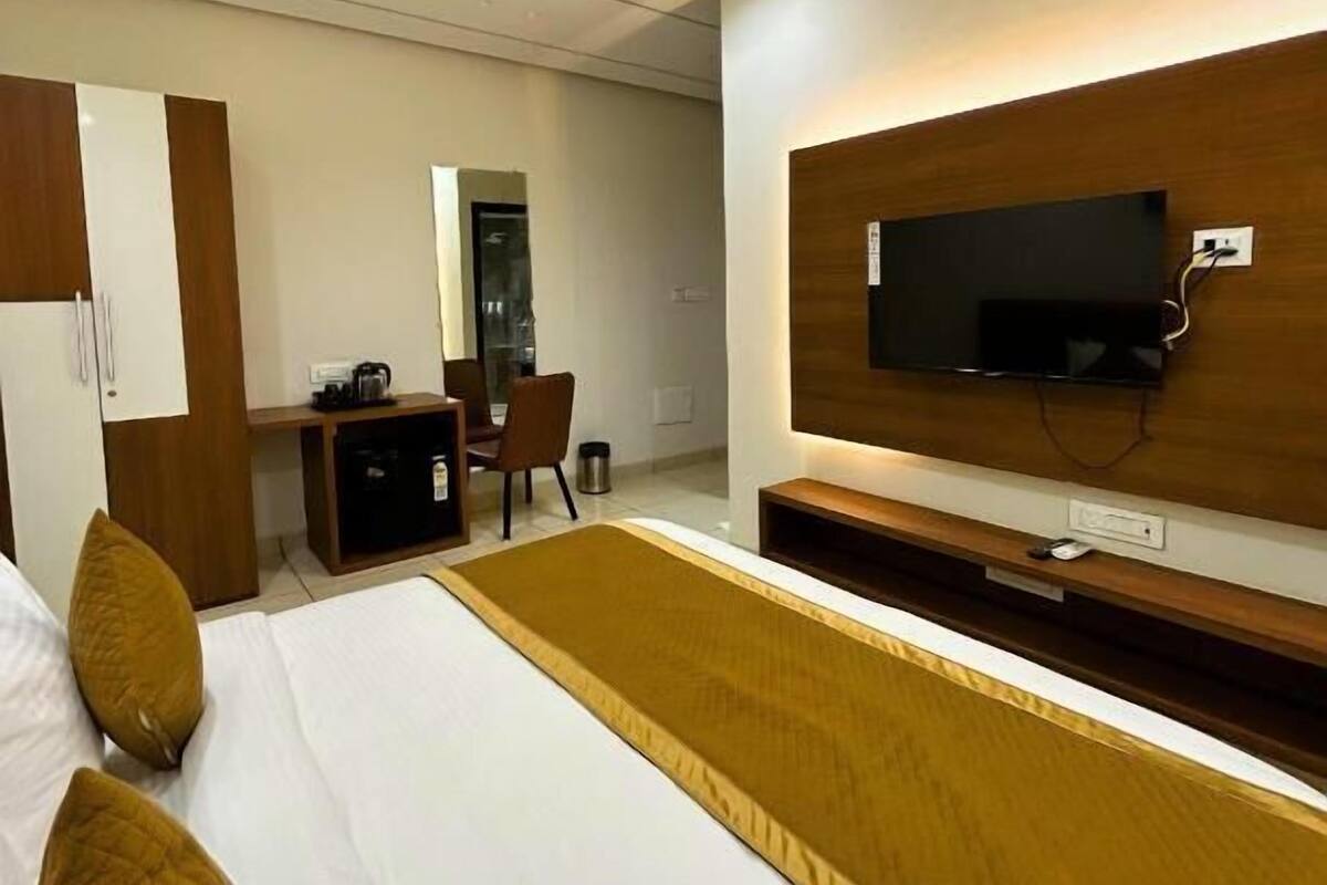 Habitación de hotel con cama, escritorio, silla, televisor montado en la pared y ventilador de techo.