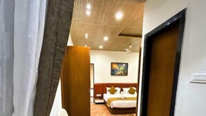 A narrow hallway with a chair, a bed with pillows, and a wooden door. - Serene-Restaurant Rooms and Banquet (Indore)