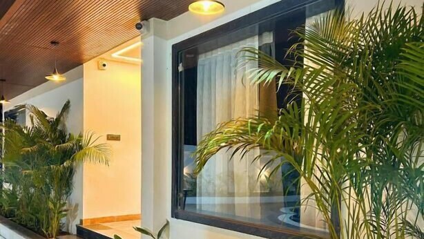A modern hotel corridor with a wooden ceiling, potted plants, and a large window with curtains. - Serene-Restaurant Rooms and Banquet (Indore)