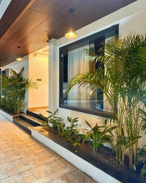Un pasillo moderno de hotel con techo de madera, plantas en macetas y un ventanal con cortinas.