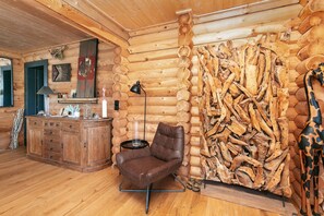Ein Blockhaus-Interieur mit einem Holzschrank, einem Ledersessel und einer Wand aus gestapelten Baumstämmen.