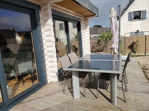 Un espace de restauration extérieur moderne, doté d’une table et de chaises en verre, d’une terrasse en bois et offrant une vue sur le quartier environnant.