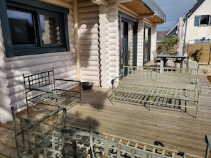 Une cabane en rondins avec une terrasse en bois, des chaises en métal et une table.