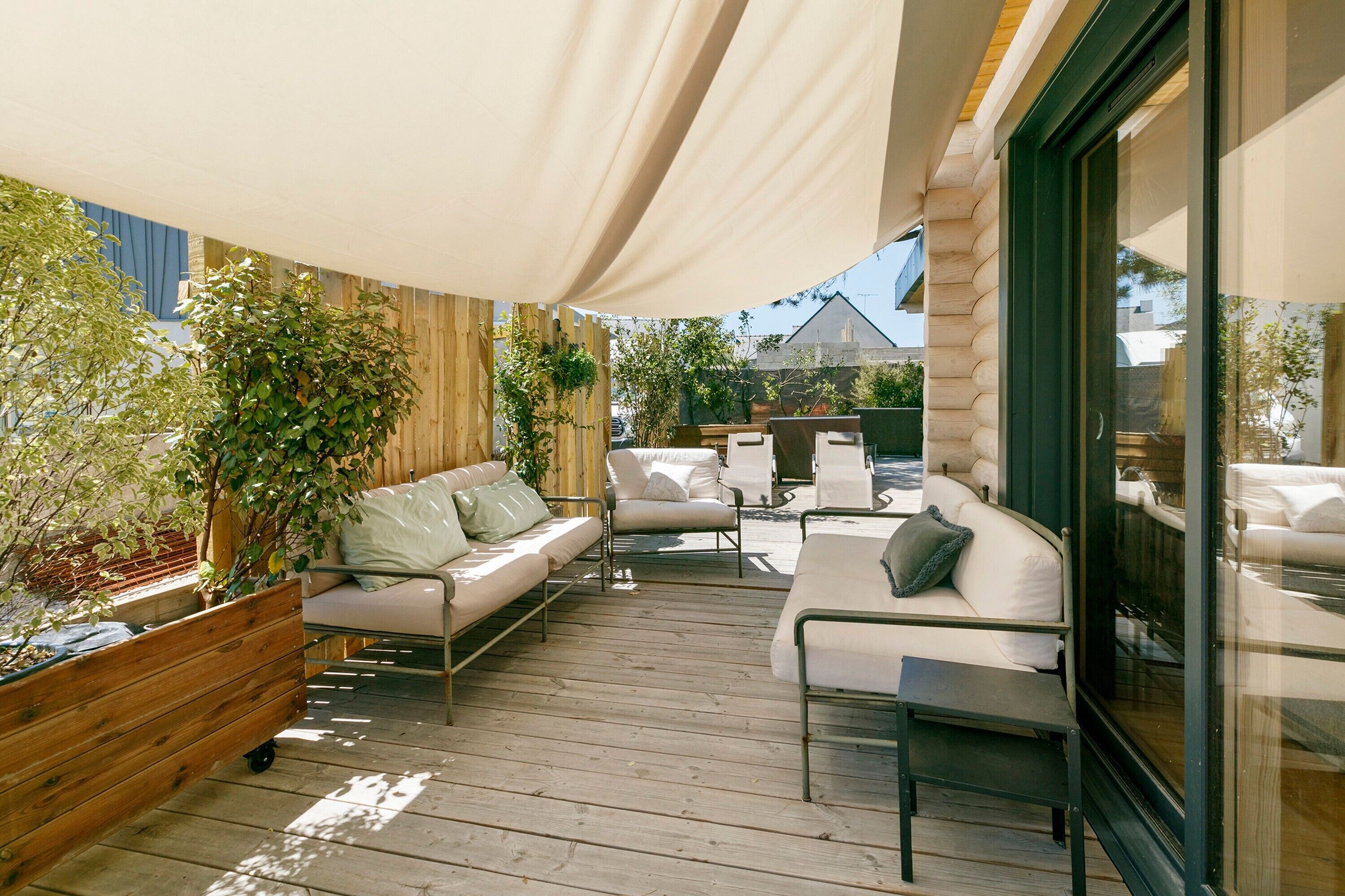 Un patio al aire libre con terraza de madera, sofás blancos y un gran paraguas que da sombra.