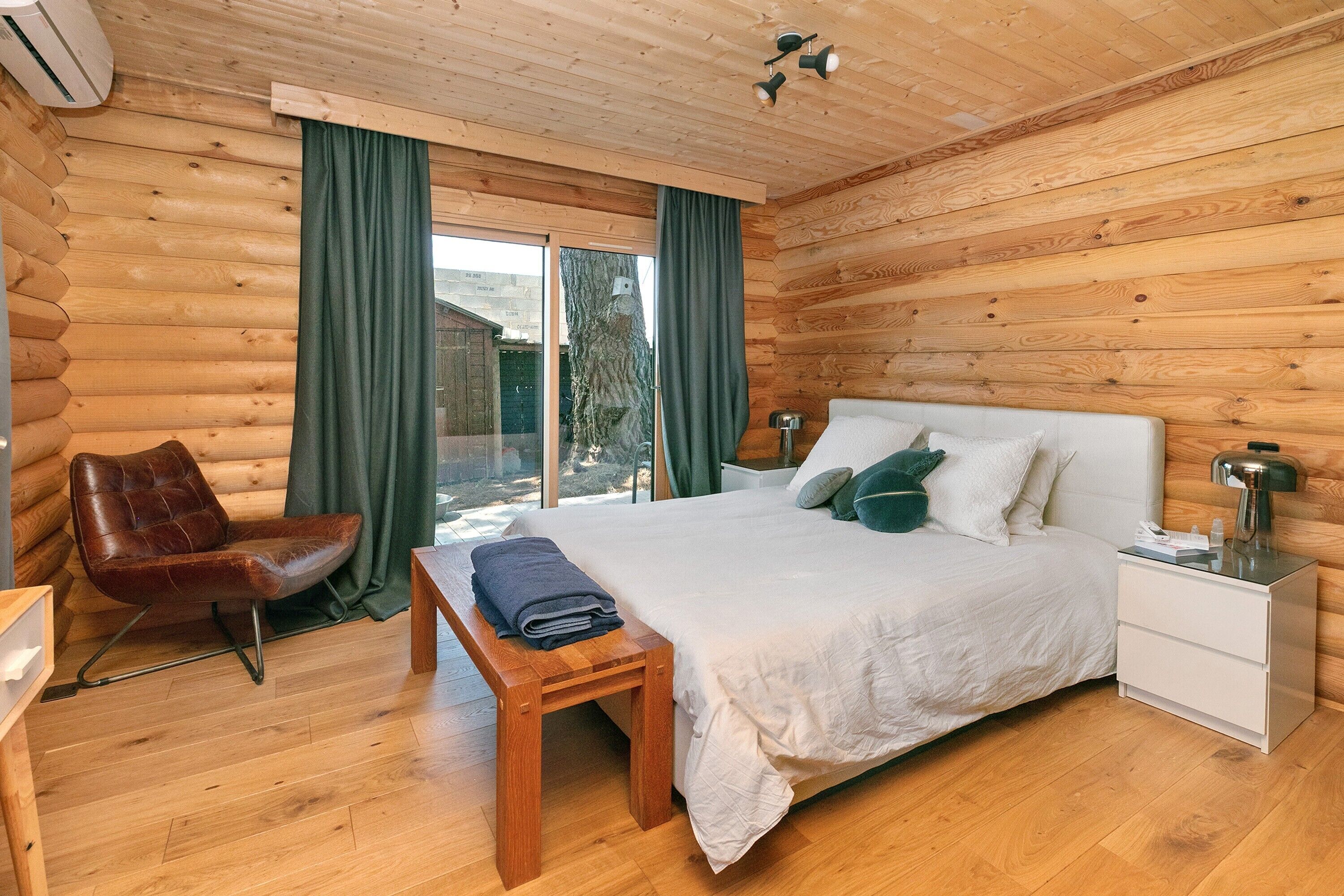 A log cabin bedroom with a bed, a chair, a nightstand, and a bench.