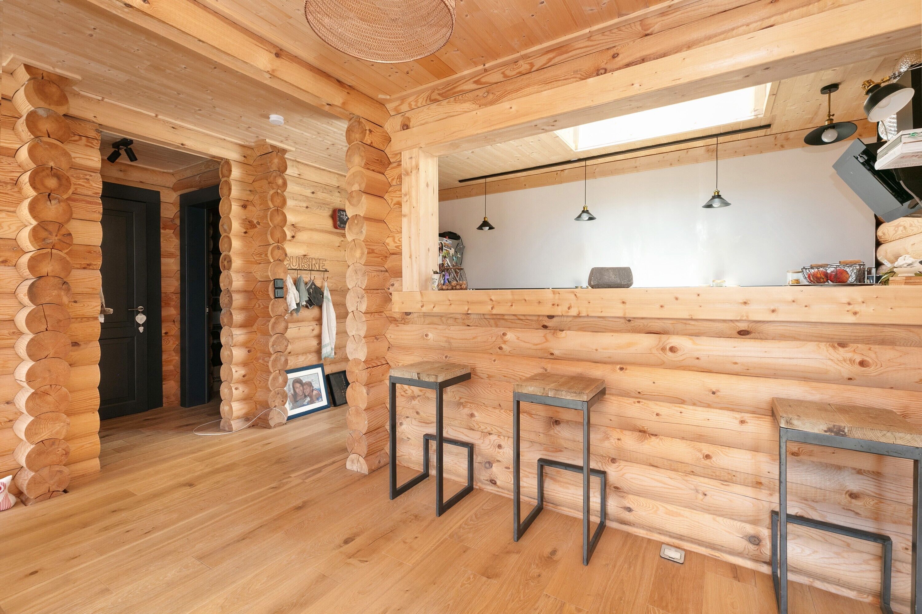 L’intérieur d’une cabane en rondins comprend un coin cuisine, des murs en bois et un espace repas avec des tabourets.