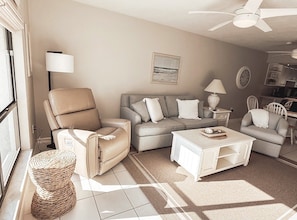 A living room with a sofa, armchair, coffee table, lamp, and a ceiling fan. - Runaway Bay 258 - Beach, Bay, Pool, Pickleball (Bradenton Beach)