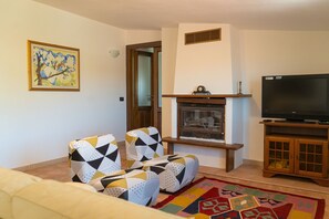 A living room with a fireplace, a television, and patterned armchairs. - Cucca's Home - Three Bedroom Apartment, Sleeps 5 (Siniscola)