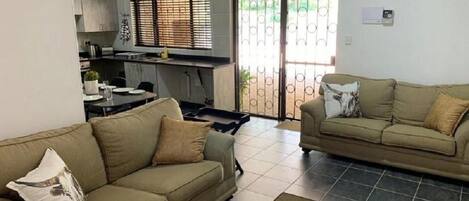 Ein Wohnzimmer mit einer Couch, einem Couchtisch und einer Küchenzeile mit Esstisch und Schränken.
