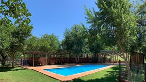 A backyard with a swimming pool, surrounded by trees and a brick wall. - Spacious 2-bedroom Apartment With Garden View in Hartbeespoort (Hartbeespoort)