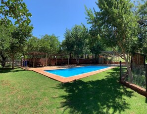 Ein Garten mit Schwimmbad, umgeben von Bäumen und einer Ziegelmauer.