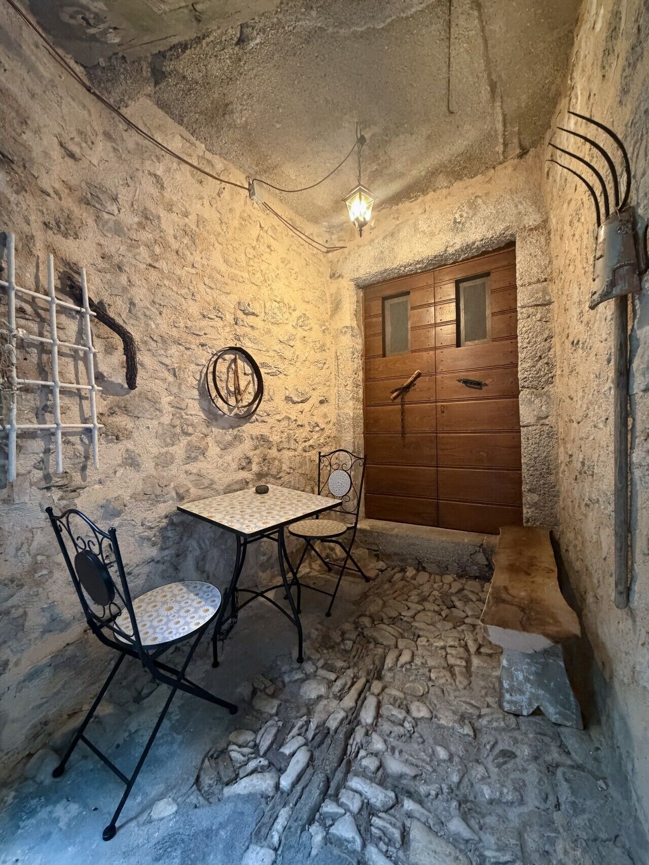 A stone-walled room with a wooden door, a metal-framed table, and two chairs.