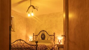 Quarto com cama, mesas de cabeceira, luminária pendente e porta de madeira.