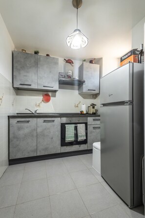 Eine moderne Küche mit grauen Schränken, einem Edelstahlkühlschrank, einer Pendelleuchte und einer gefliesten Spritzschutzwand.