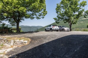 Ein gepflasterter Parkplatz mit zwei Autos, umgeben von Bäumen und einer Steinmauer.