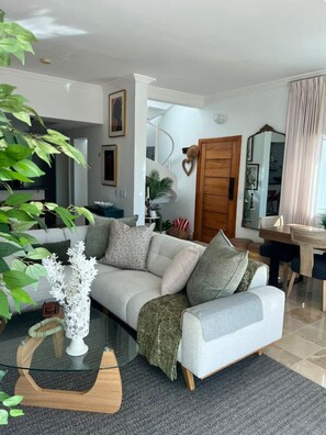 Ein Wohnzimmer mit einer Couch, einem Glastisch und einem Essbereich mit Tisch und Stühlen.