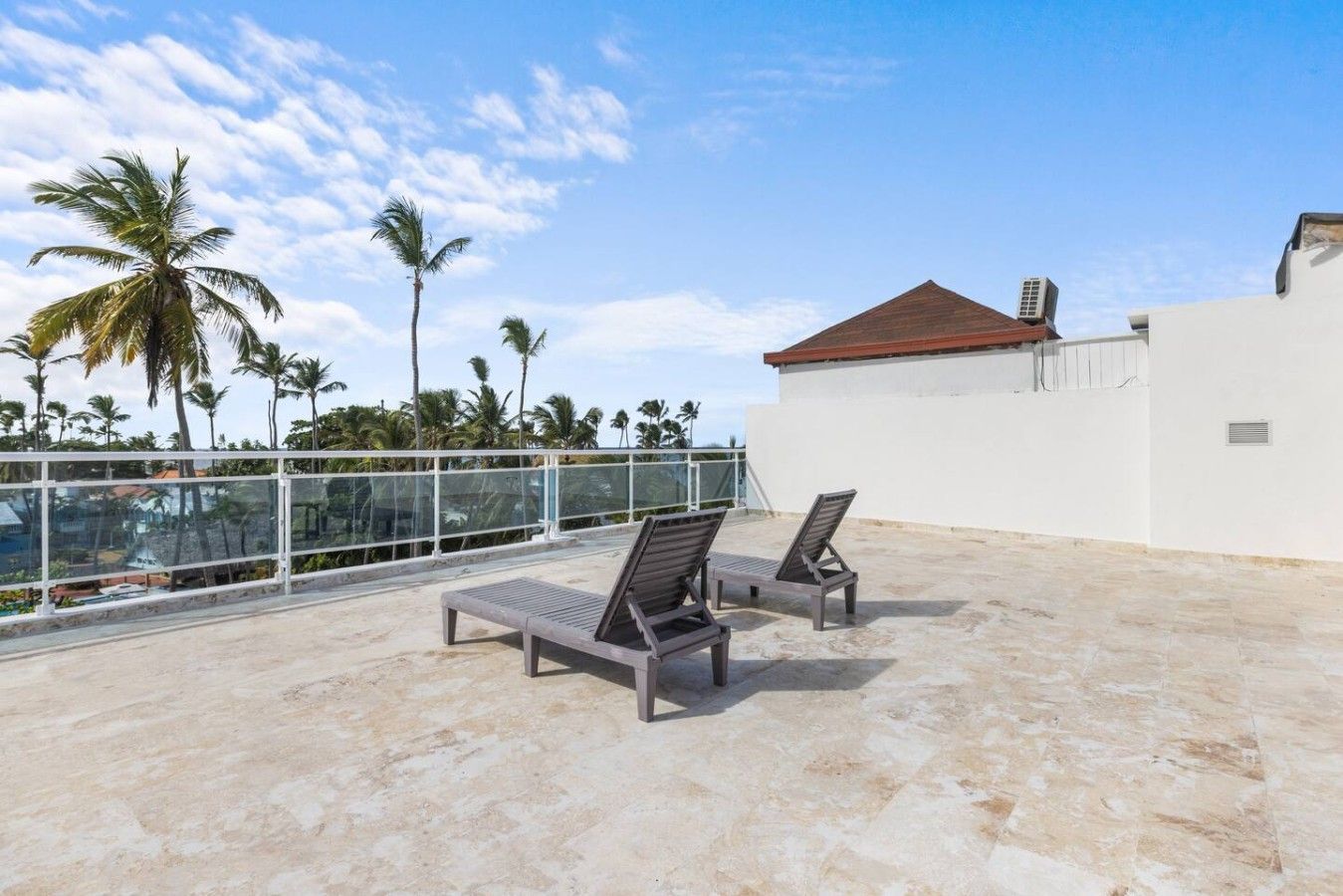 A rooftop terrace with two lounge chairs, a white wall, and a red roof.