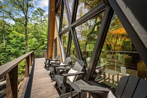A wooden deck with outdoor seating and large windows overlooking a forest. - Luxe A-Frame | Golf · Hot Tub · National Forest (Morganton)