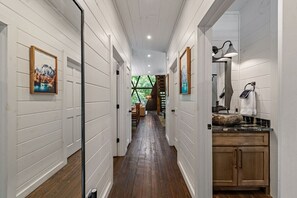 A hallway with wooden walls and a wooden floor leading to a bathroom with a sink and cabinets. - Luxe A-Frame | Golf · Hot Tub · National Forest (Morganton)