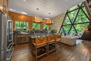Eine moderne Küche mit Kochinsel, Holzschränken und großem Fenster mit Blick auf einen Wald.