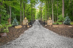 Ein Kiesweg führt durch ein bewaldetes Gebiet, vorbei an einem steinernen Tor und einem Schild, das den Deerbird Trail weist.
