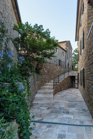 Ein schmaler Steinweg, gesäumt von Gebäuden mit Steinmauern und grünen Fensterläden, der zu einer Treppe führt.