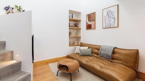 A modern living room with a brown leather sofa, a small ottoman, a bookshelf, and two framed artworks on the wall. - URBAN LOFT PORTO (Porto)